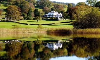 a large white house is situated on a hillside overlooking a body of water , with trees in the background at Ees Wyke Country House