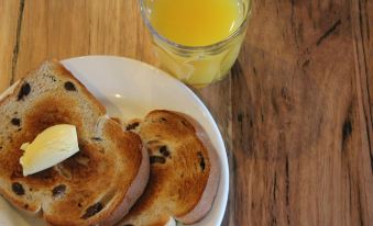 a plate of bread with butter and a glass of orange juice on a wooden table at Alexandra Place