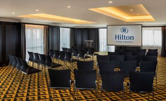 a large conference room with rows of chairs arranged in a semicircle , and a projector screen mounted on the wall at Hilton Vienna Plaza