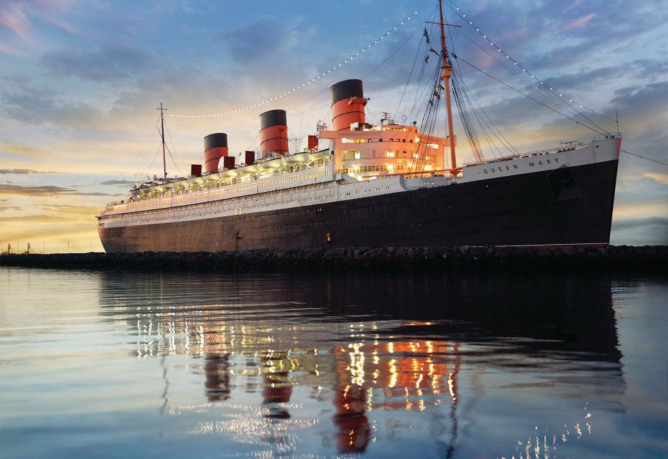 a large , red and white queen elizabeth ii cruise ship docked at a harbor during sunset at The Queen Mary