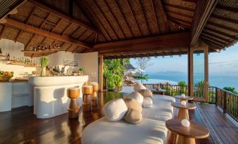 a luxurious beachfront resort with wooden furniture , including a lounge area and dining table , overlooking the ocean at Six Senses YAO Noi