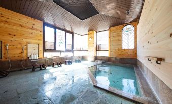 a modern , wooden interior with large windows and a sunken pool , surrounded by stone flooring at Shima Onsen Kashiwaya Ryokan