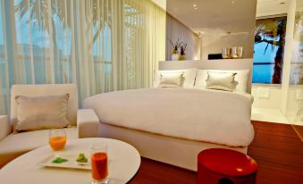 a large bed with white linens is in a room with a red ottoman and a coffee table at Renaissance Barcelona Fira Hotel
