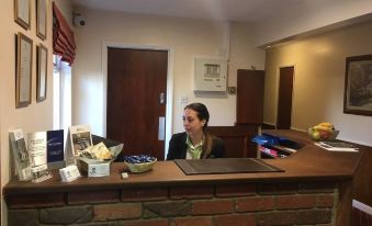 a woman standing behind a reception desk in a hotel lobby , talking on the phone at The Cedars Hotel