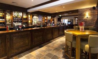 a bar with a wooden counter and chairs , as well as a variety of bottles on display at Premier Inn Grantham