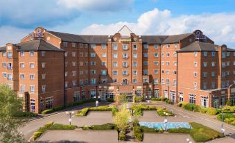 a large brick building with multiple floors and a courtyard in front of it , surrounded by trees at Doubletree by Hilton Dartford Bridge