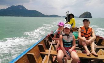 a group of people , including children , are enjoying a boat ride on the ocean , surrounded by mountains and the ocean at Lam-Tong Resort