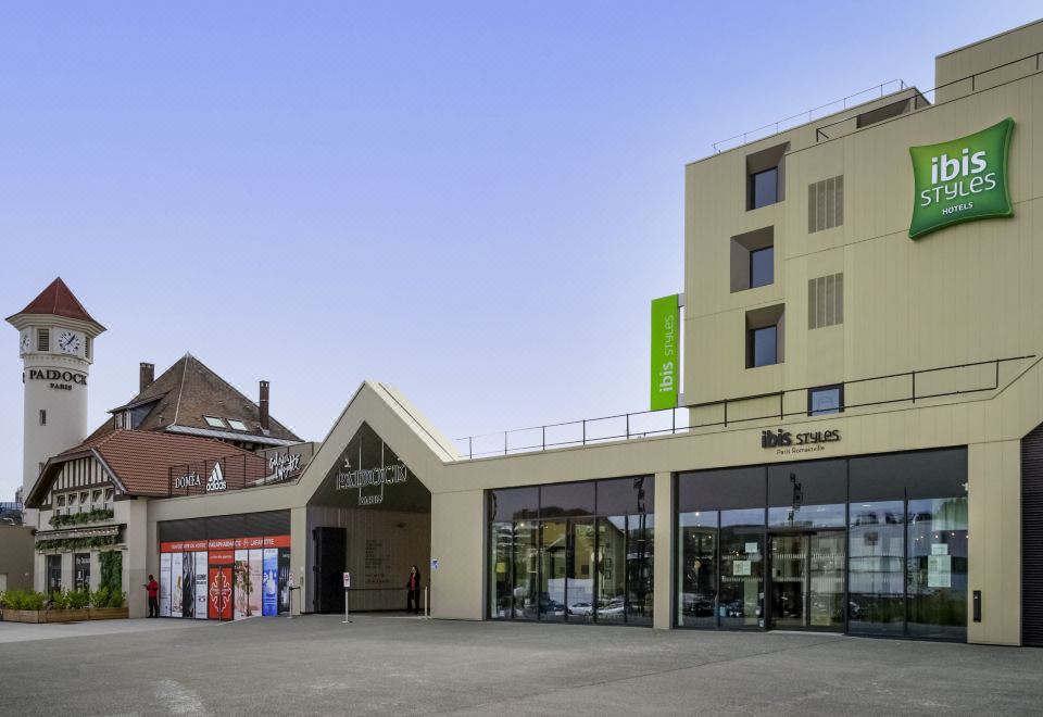a modern building with a green sign and a smaller one with a sign on top at Ibis Styles Paris Romainville