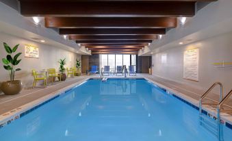 an indoor swimming pool with a wooden ceiling , surrounded by lounge chairs and yellow chairs at Home2 Suites by Hilton Dekalb