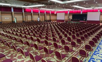 a large , empty conference room with rows of red and gold chairs arranged in an auditorium - like setting at Grand Asrilia Hotel