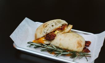 a sandwich with meat and cheese is placed on a piece of paper with a sprig of rosemary at Under Canvas Mount Rushmore