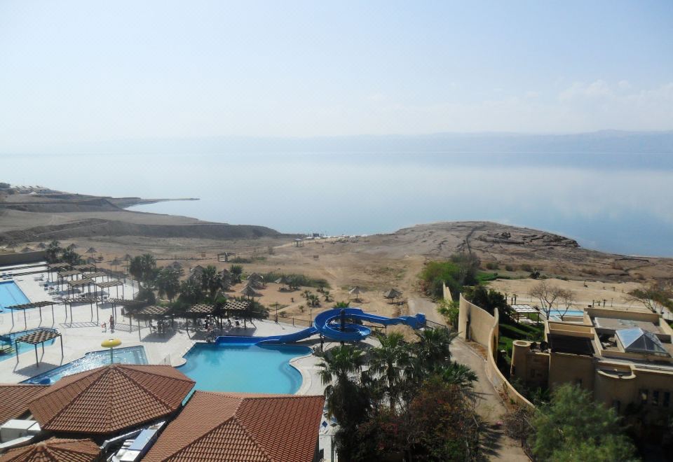 a resort with a large pool surrounded by a sandy beach , where people are enjoying their time at Dead Sea Spa Hotel