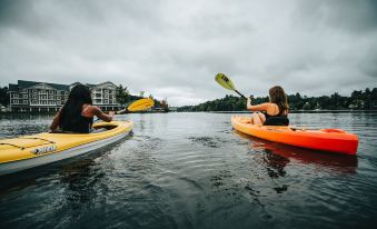 two women are paddling in a yellow and orange kayak on a lake , enjoying their time together at Saranac Waterfront Lodge, Trademark Collection by Wyndham
