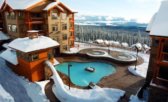 a large , well - maintained swimming pool surrounded by snow - covered buildings and a hotel building in the background at Sundance Resort