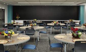 a dining area with several round tables and chairs , each set for a meal , under a blackboard wall at Aloft Seattle Redmond