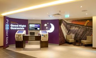 a hotel lobby with a check - in desk , a computer monitor , and a staircase leading to an upstairs area at Premier Inn Trowbridge