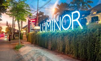 "a city street with a large blue neon sign that reads "" luminor "" prominently displayed on the sidewalk" at Luminor Hotel Jember by WH