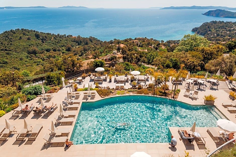 a large outdoor pool surrounded by lounge chairs and umbrellas , with a view of the ocean in the background at Hotel la Villa Douce