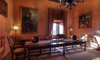 a room with a long wooden table and chairs , large paintings on the walls , and a chandelier at Parador de Jarandilla