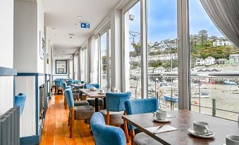 a modern restaurant with large windows overlooking the sea , featuring blue chairs and wooden tables at Portbyhan Hotel