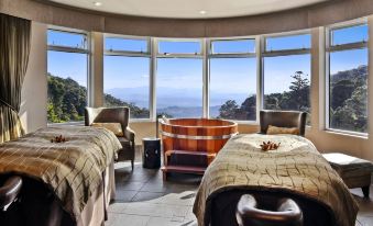 a room with two beds and a hot tub , surrounded by windows that offer a view of the mountains at O'Reilly's Rainforest Retreat