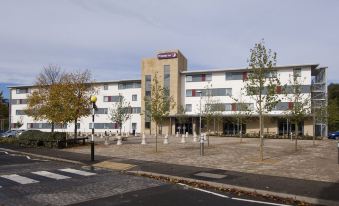 a large building with a red sign on top is surrounded by trees and a street at Premier Inn Rochester