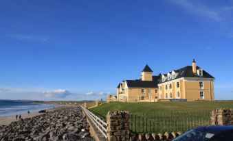a large building is situated on the shore of a beach , with a stone wall in front of it at Sandhouse Hotel