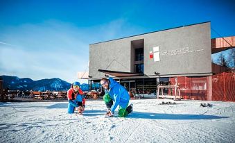 a man and a young girl are standing on a snow - covered hill in front of a building , preparing to ski down the slope at Spaces Hotel