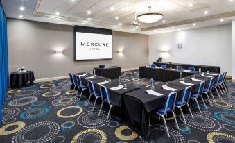 "a large conference room with multiple tables and chairs , a screen displaying the word "" mercury ,"" and a projector screen on the wall" at Mercure Telford Centre Hotel