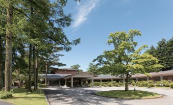 a large building with a red roof is surrounded by trees and has a parking lot in front of it at Karuizawa Prince Hotel East