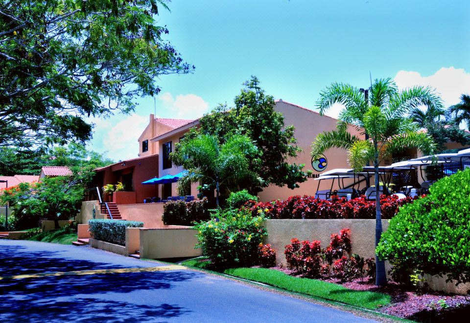 a brick building with a red roof , surrounded by lush green trees and bushes , under a clear blue sky at Park Royal Homestay Club Cala Puerto Rico