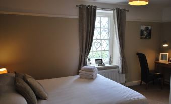 a cozy bedroom with a white bed , grey curtains , and a window looking out onto a city street at The Punchbowl Hotel