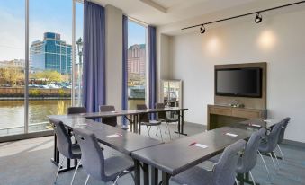 a conference room with a large table and chairs , a tv on the wall , and blue curtains at Aloft Milwaukee Downtown