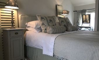 a cozy bedroom with a large bed , white bedding , and striped pillows , along with a nightstand and lamp at Radnor House