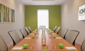 a long wooden table with green apples and water bottles , set up for a meeting in a conference room at Home2 Suites by Hilton Dekalb