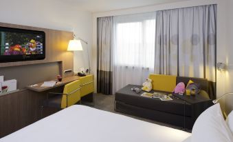 a hotel room with a bed , couch , tv , and desk , all decorated in a modern style at Novotel Leuven Centrum