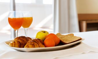 a breakfast tray filled with various food items , including croissants , apples , oranges , and bread , placed on a dining table at Hotel Fontana Plaza
