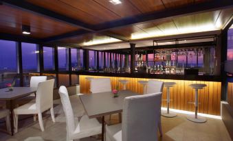 a modern bar with white chairs and tables , wooden paneling , and a bar area lit by lights at ASTON Imperial Bekasi Hotel & Conference Center