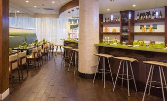 a modern bar with wooden floors , white walls , and green accents , containing various bottles and glasses at Aloft Miami Dadeland