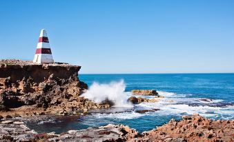 a lighthouse standing on a rocky cliff overlooking the ocean , with waves crashing against the rocks at Robetown Motor Inn & Apartments