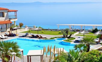 a large pool surrounded by lounge chairs and palm trees , with a view of the ocean in the background at Blue Bay Halkidiki