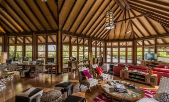 a spacious living room with wooden floors , high ceilings , and large windows that offer views of the outdoors at Four Seasons Resort Maldives at Kuda Huraa