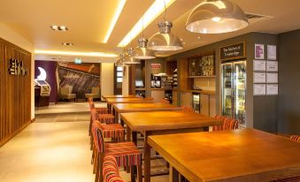 a dining area with wooden tables and chairs , surrounded by a bar and a tv at Premier Inn Trowbridge