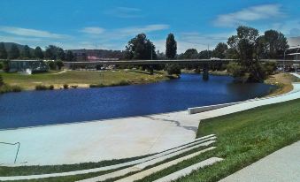 a beautiful river with a bridge in the background , surrounded by green grass and trees at Crest Motor Inn