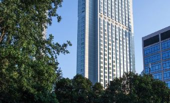 A large building with tall trees in front and a blue sky behind it at The Kunlun Jing An