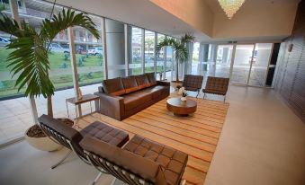 a spacious room with brown leather couches , chairs , and tables , surrounded by windows and a chandelier at Hplus Vision Executive