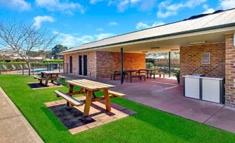 a brick house with an outdoor dining area , picnic tables , and green grass , under a blue sky at Potters Apartments