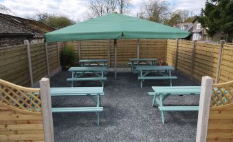 a green umbrella over a picnic table with six blue tables and wooden benches , surrounded by a wooden fence at The Punchbowl Hotel