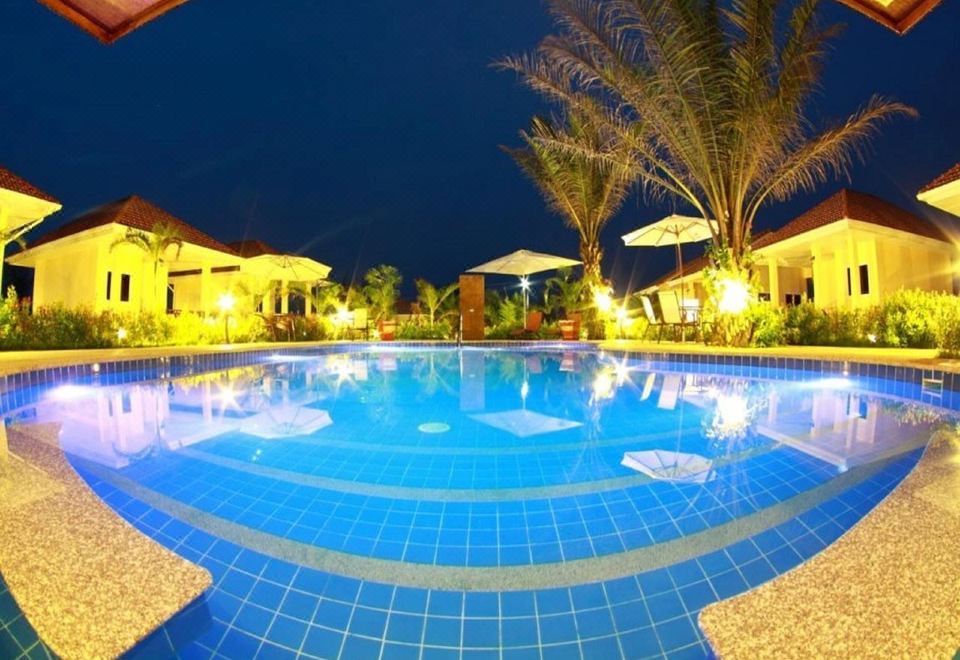 a large , well - maintained swimming pool with blue tiles and palm trees surrounding it at night at Ao Thai Resort