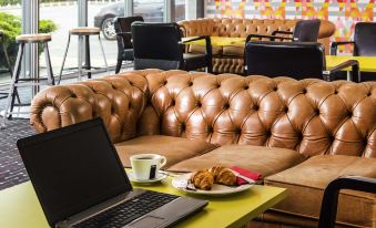 a laptop is open on a table next to a couch with pastries and coffee at Ibis Styles Barnsley